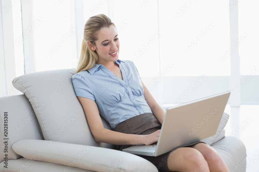 Cheerful classy businesswoman sitting on couch using her notebook Cheerful classy businesswoman sitting on couch using her notebook