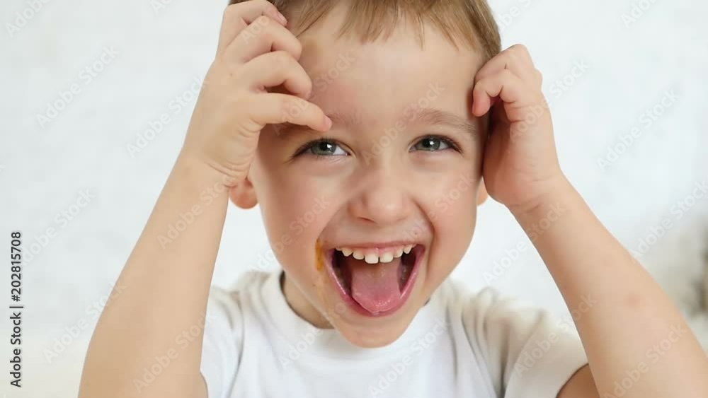 Close-up of a kid looks and smiles at the camera in slow motion. The child shows joy, shows a tongue and a broad smile Close-up of a kid looks and smiles at the camera in slow motion. The child shows joy, shows a tongue and a broad smile