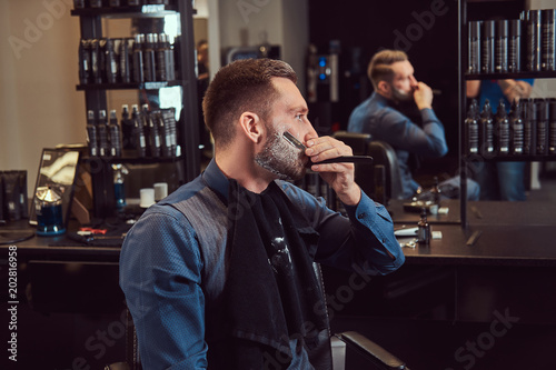 Portrait of a stylish male who himself shaving in a hairdressing salon.