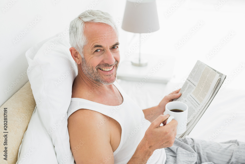 Smiling mature man with coffee cup and newspaper in bed
