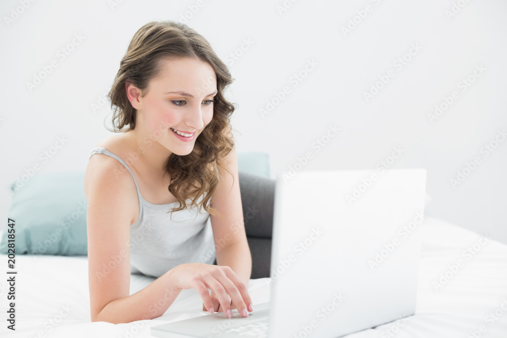 Smiling casual brunette using laptop in bed Smiling casual brunette using laptop in bed