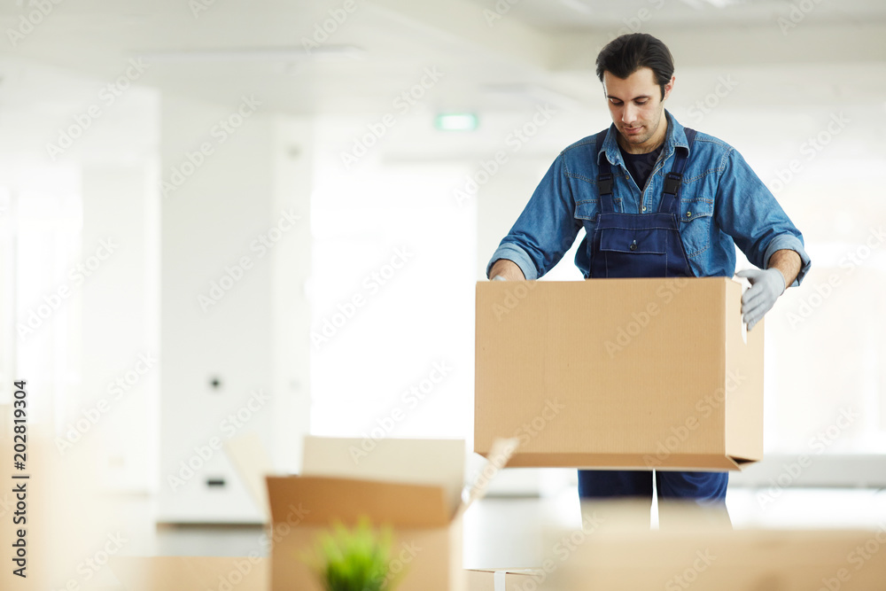 Young delivery service worker carrying packed carton boxes to new office in contemporary business center Young delivery service worker carrying packed carton boxes to new office in contemporary business center