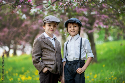 Little preschool boys, cute children, brothers, dressed in vintage style clothes, in a park under blooming trees, looking fashionable