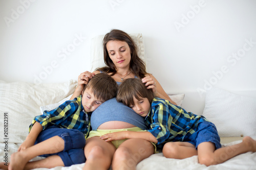 Young pregnant mother, lying in bed, reading a book to her two older children