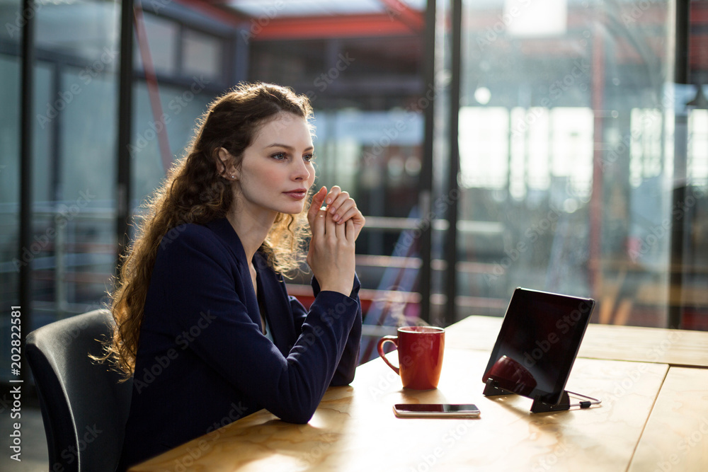 Thoughtful business executives sitting with digital tablet and cup of coffee on table Thoughtful business executives sitting with digital tablet and cup of coffee on table