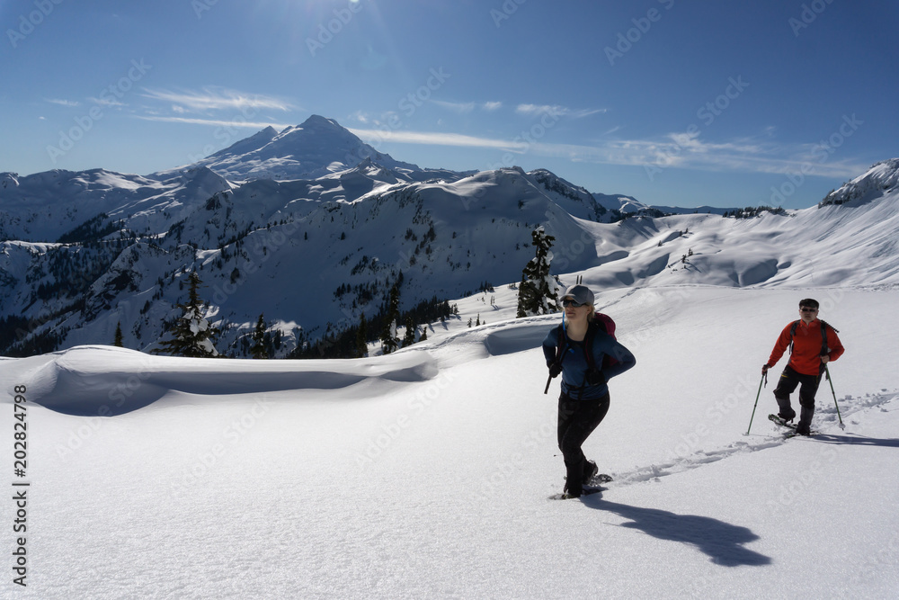 Adventurous man and woman are snowshoeing in the snow. Taken in Artist Point, Northeast of Seattle, Washington, United States of America.