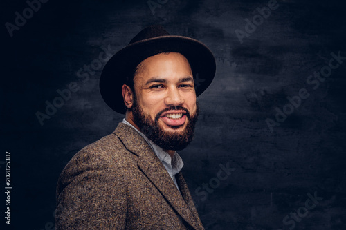 Studio portrait of a smiling handsome Afro-American male in an elegant brown jacket and hat.