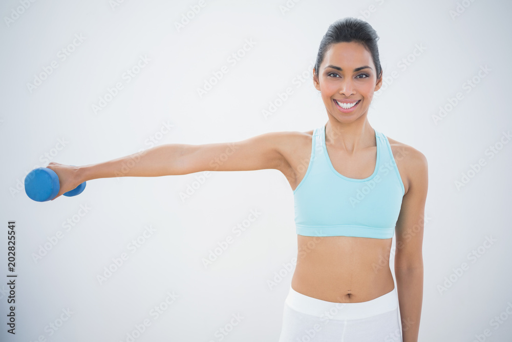 Slender dark haired woman lifting blue dumbbell