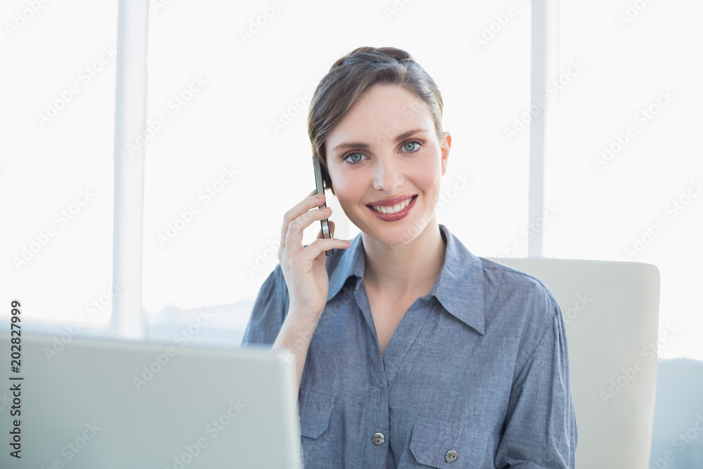 Friendly young secretary phoning with her smartphone sitting at her desk Friendly young secretary phoning with her smartphone sitting at her desk