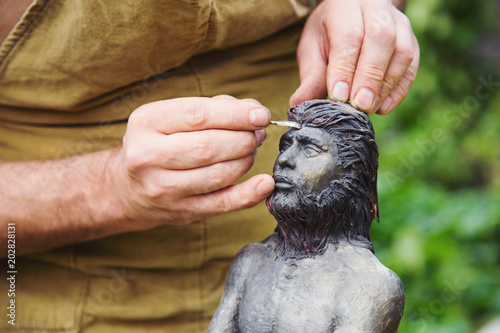 Closeup hands of sculptor in apron making sculpture of man using instrument outdoor