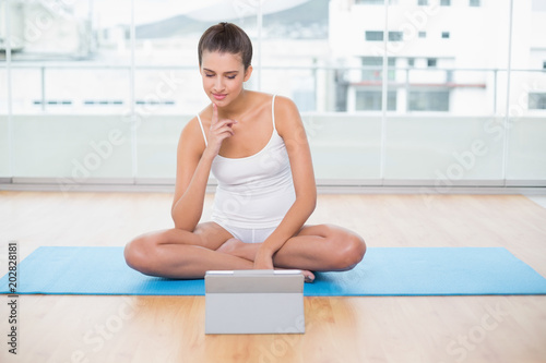 Concentrated natural brown haired woman in white sportswear looking at a tablet pc