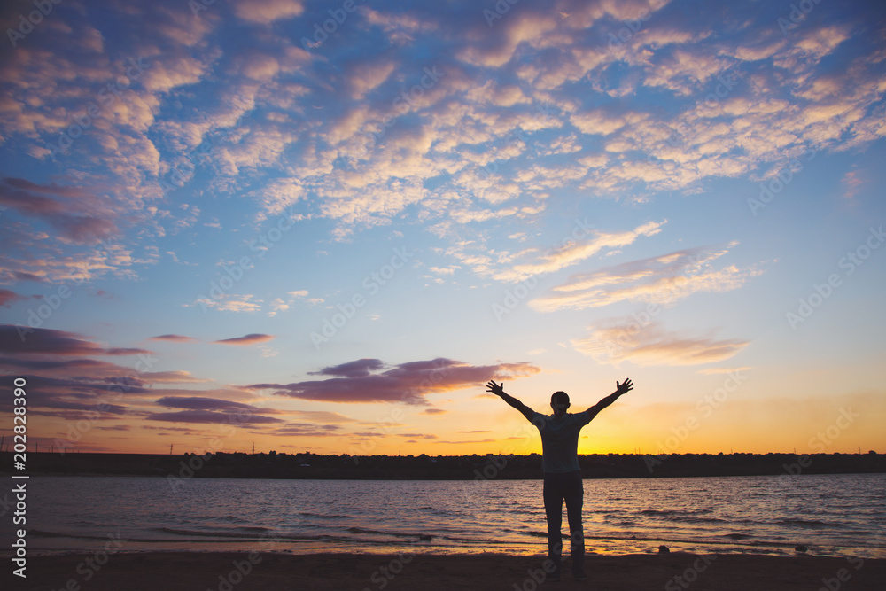Silhouette of man with arms outstretched against cloudy sky on sunset near lake