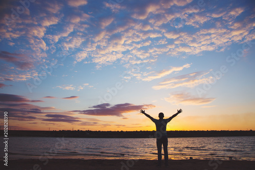 Silhouette of man with arms outstretched against cloudy sky on sunset near lake © alexaphotoua