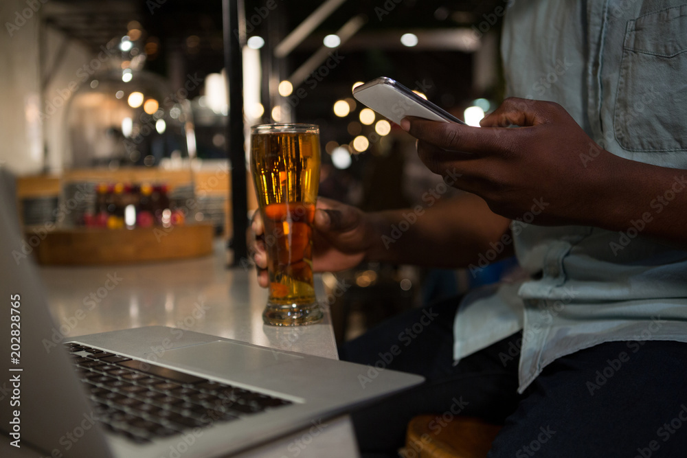 Mid section of man using mobile phone while having beer