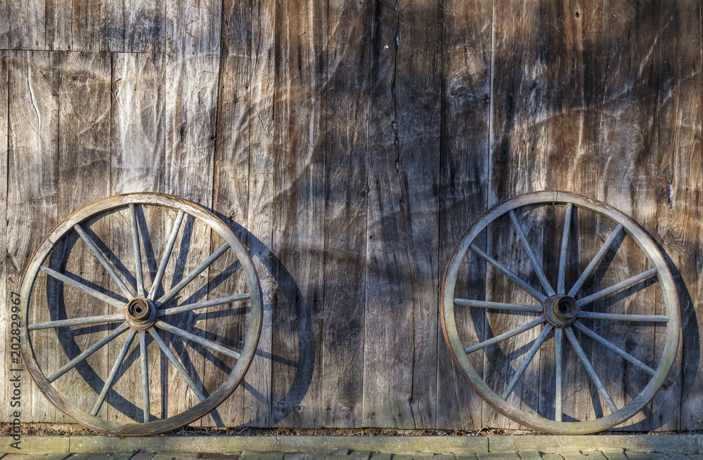 Zwei Wagenräder lehnen an einer Scheunenwand