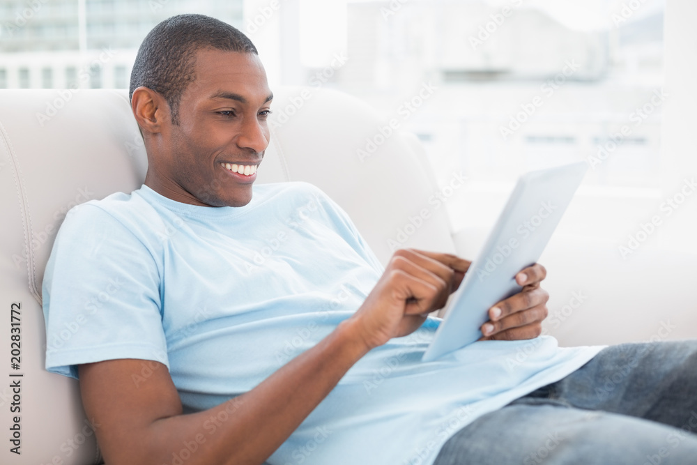 Casual smiling young Afro man using digital tablet on sofa