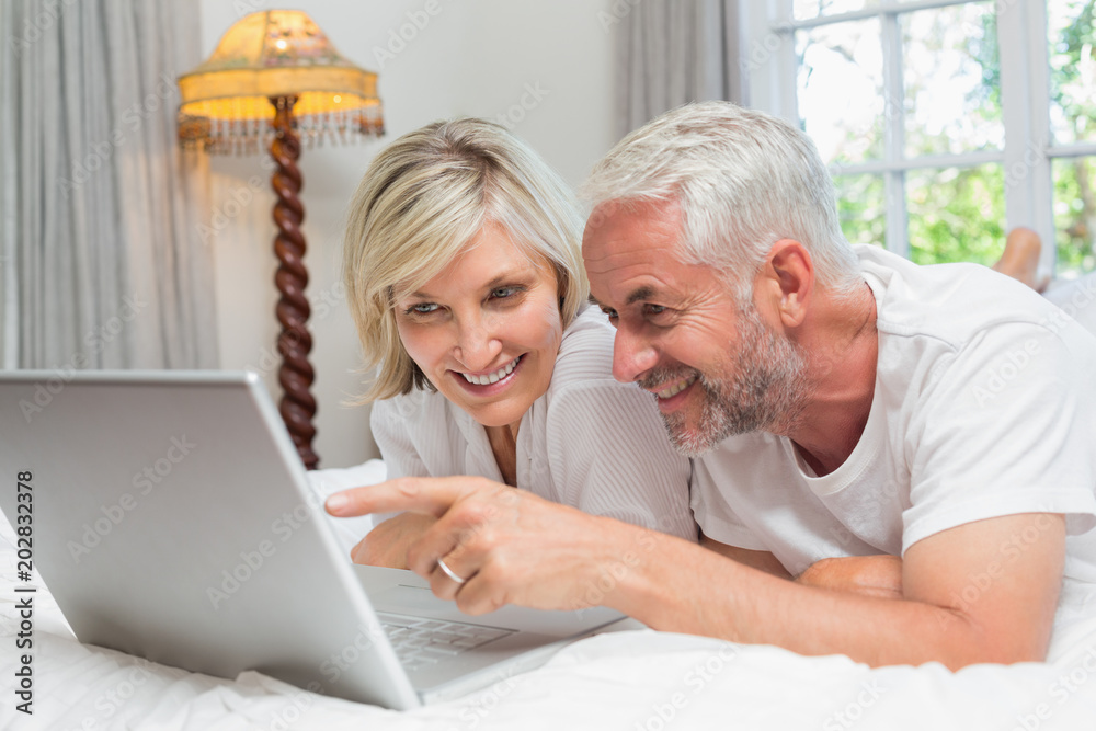 Happy mature couple using laptop in bed Happy mature couple using laptop in bed