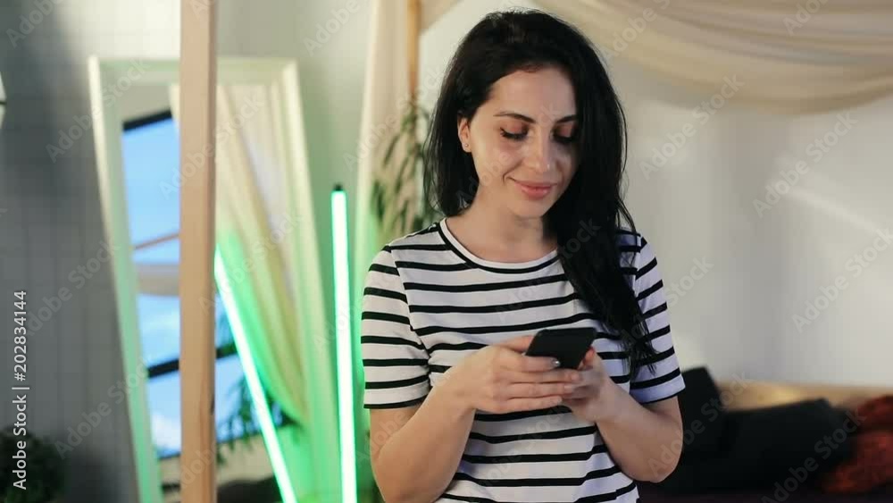 cheerful smiling woman using smartphone inside home interior on background front view smiling friendly face checking notification social networking online typing message internet connect wifi 3G cheerful smiling woman using smartphone inside home interior on background front view smiling friendly face checking notification social networking online typing message internet connect wifi 3G