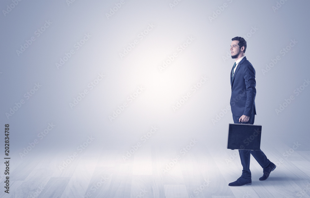 Successful businessman walking in front of an empty wall with briefcase on his hand
Successful businessman walking in front of an empty wall with briefcase on his hand