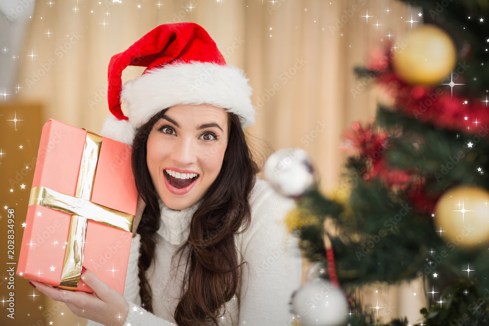 Surprised brunette holding a gift against twinkling stars Surprised brunette holding a gift against twinkling stars