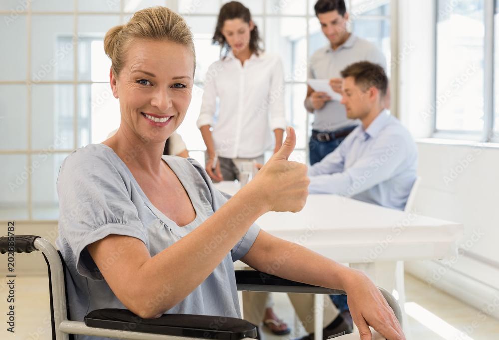 Casual businesswoman in wheelchair smiling at camera with team behind her Casual businesswoman in wheelchair smiling at camera with team behind her