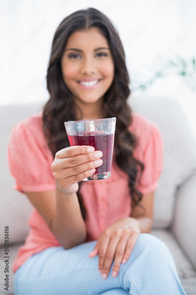 Smiling cute brunette sitting on couch holding glass of juice