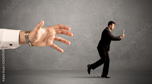 Young miniature businessman running from a big hand with light grey background