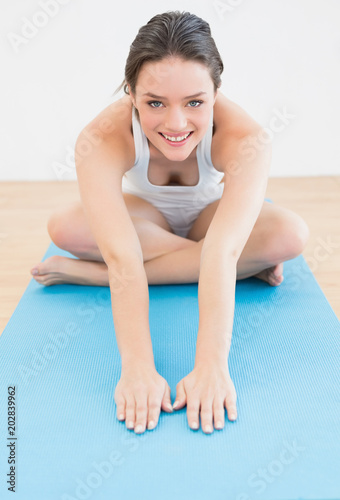 Smiling sporty woman stretching hands on exercise mat