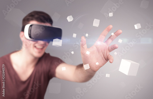 Young impressed man wearing virtual reality goggles with grey cubes around him 
