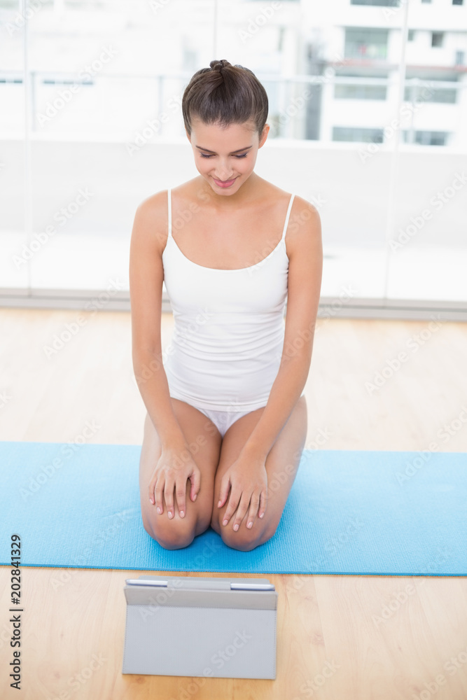 Attentive natural brown haired woman in white sportswear looking at a tablet pc Attentive natural brown haired woman in white sportswear looking at a tablet pc