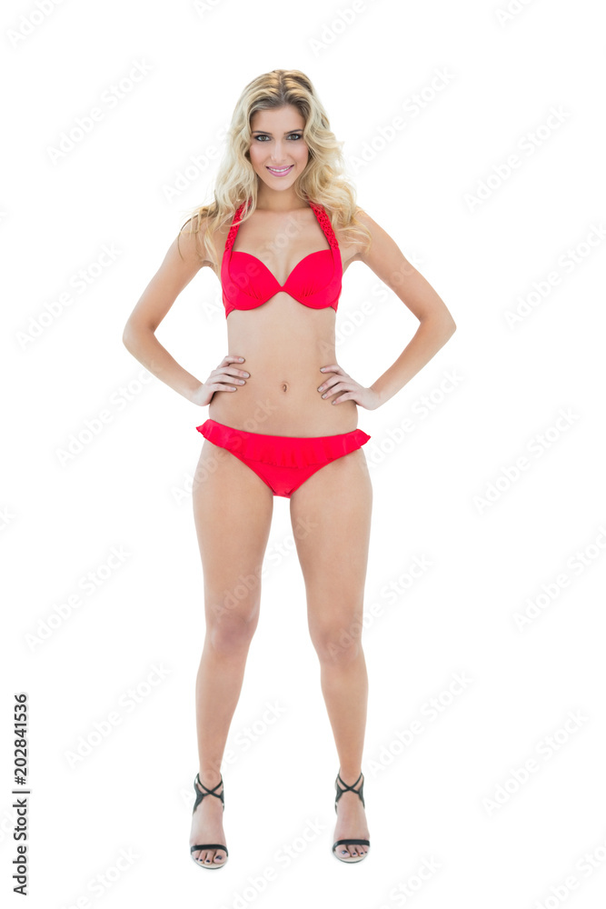 Cheerful smiling blonde model posing with hands on hips wearing red bikini Cheerful smiling blonde model posing with hands on hips wearing red bikini
