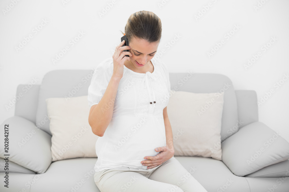 Young pregnant woman phoning while holding her belly and looking at it Young pregnant woman phoning while holding her belly and looking at it