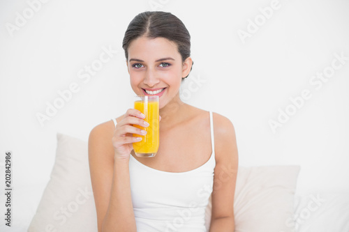 Pretty young brown haired model in white pajamas drinking orange juice