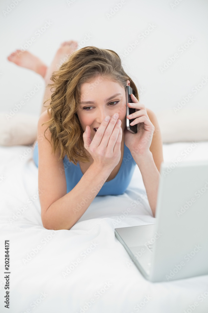 Beautiful young woman lying on her bed phoning with her smartphone Beautiful young woman lying on her bed phoning with her smartphone