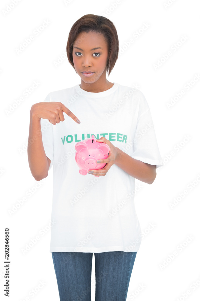 Serious volunteer woman pointing at her piggy bank Serious volunteer woman pointing at her piggy bank