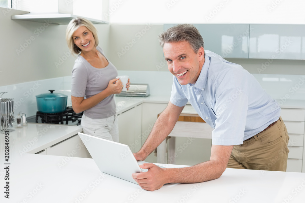 Obraz premium Happy man and woman with laptop in the kitchen