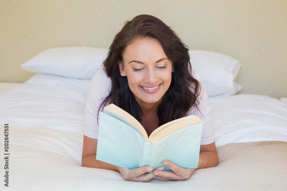Smiling woman reading book while lying in bed Smiling woman reading book while lying in bed