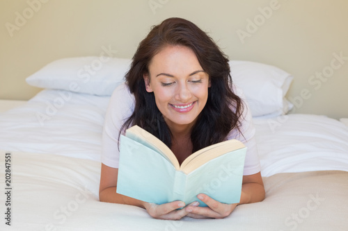 Smiling woman reading book while lying in bed