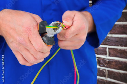Electrician cutting wire with pliers against red brick wall
