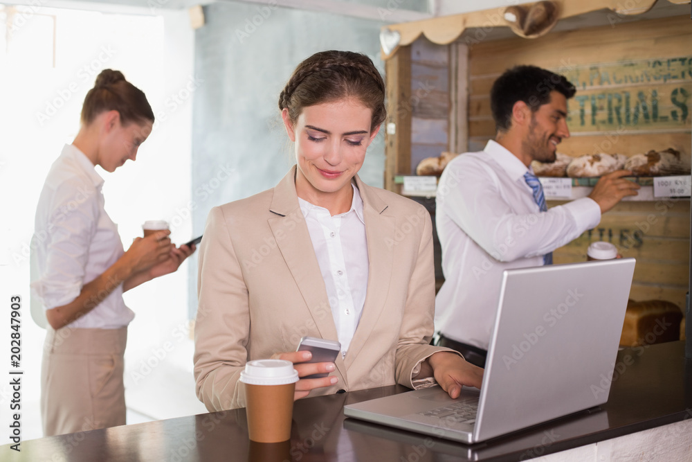 Businesswoman using mobile phone and laptop in office cafeteria Businesswoman using mobile phone and laptop in office cafeteria