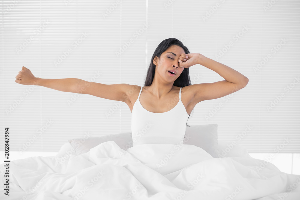 Lovely tired woman stretching out while sitting on her bed Lovely tired woman stretching out while sitting on her bed