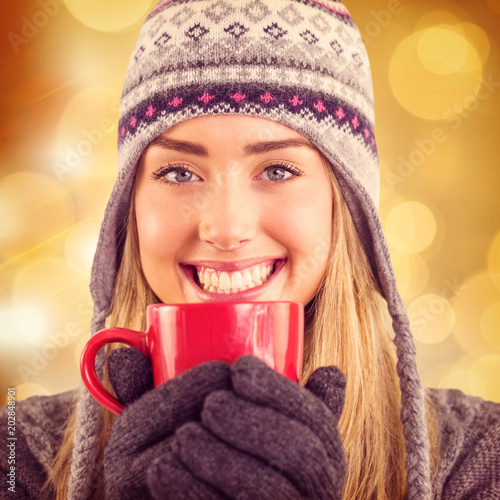 Happy blonde in winter clothes holding mug against glowing background