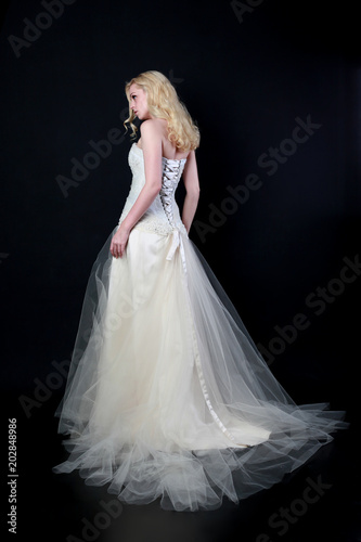 full length portrait of woman wearing white bridal gown. standing poison black studio background. © faestock