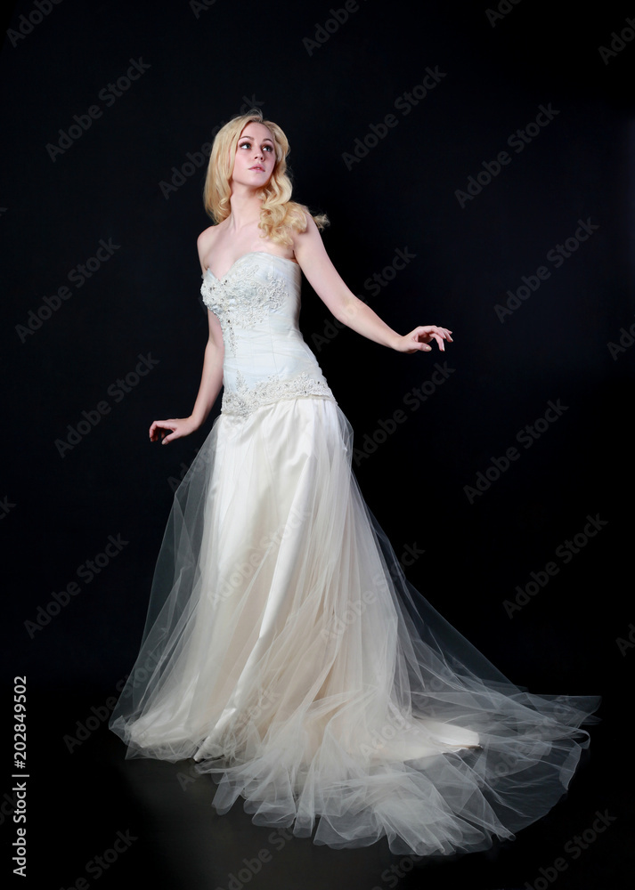 full length portrait of woman wearing white bridal gown. standing poison black studio background.