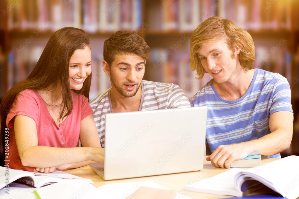 College students using laptop in library against books on desk in library College students using laptop in library against books on desk in library