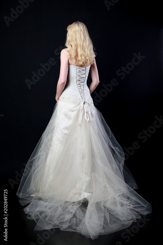 full length portrait of woman wearing white bridal gown. standing poison black studio background.