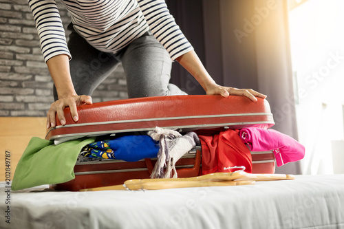  Woman trying to fit all clothing to packing her red suitcase before vacation. photo