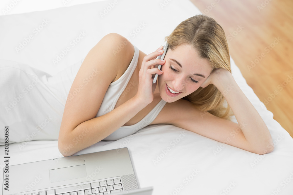 Obraz premium Peaceful blonde woman phoning while lying on her bed 