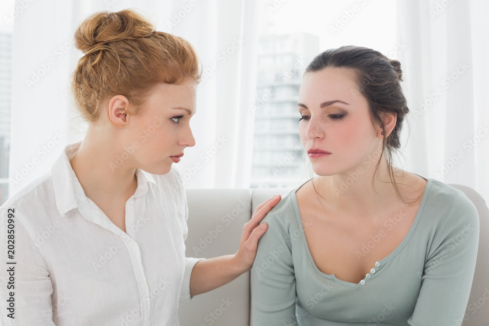 Young woman consoling female friend sitting on sofa Young woman consoling female friend sitting on sofa