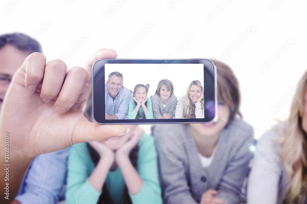 Hand holding smartphone showing against cute family lying on the floor smiling at camera